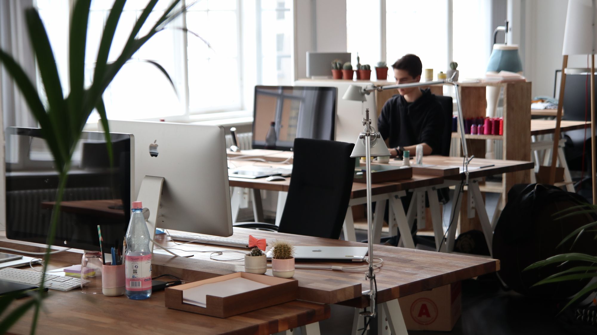 A daylit studio of oak trestle desks, used as atmosphere for a small practice