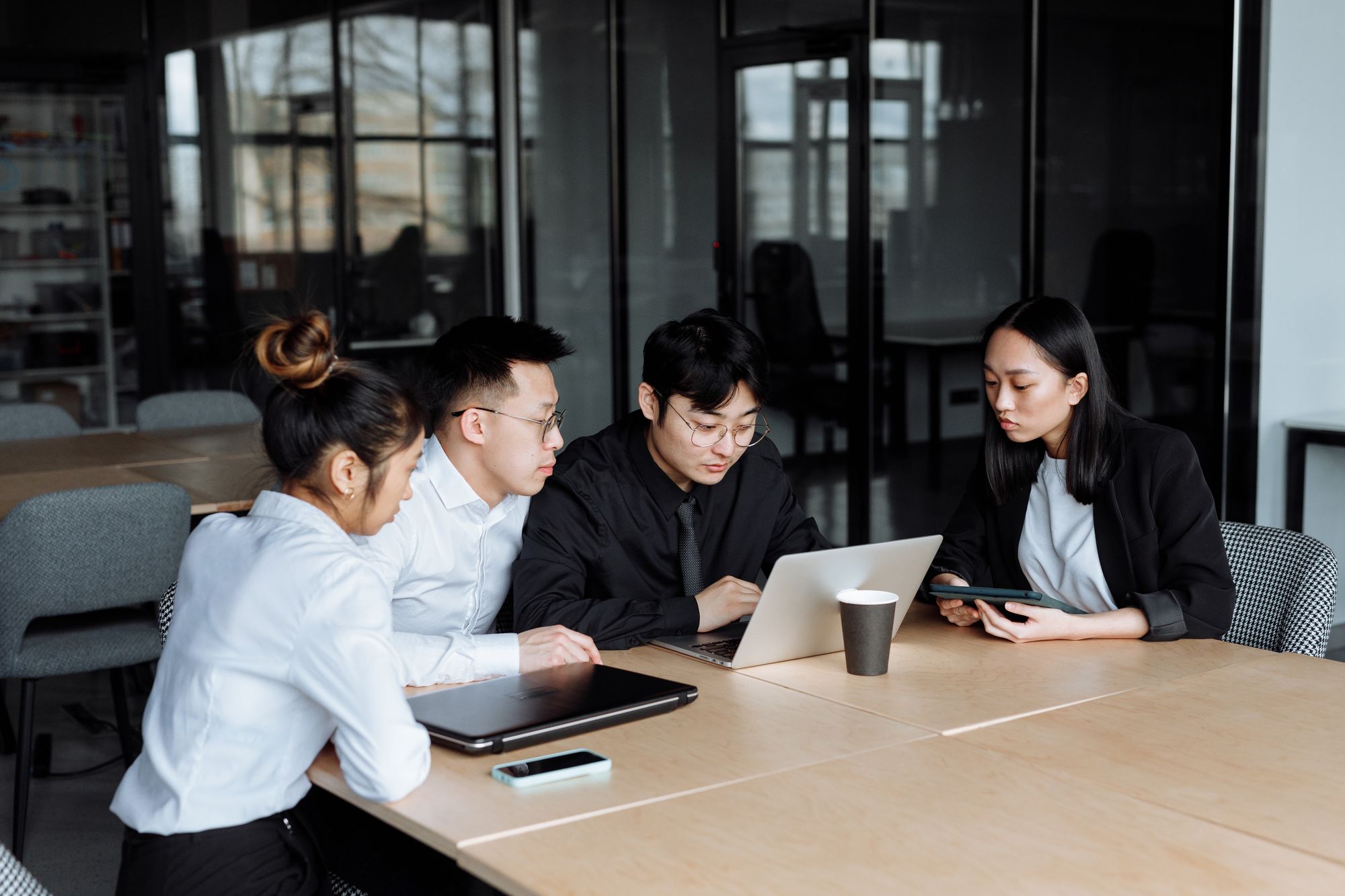 Four people gathered at a pale table around one laptop