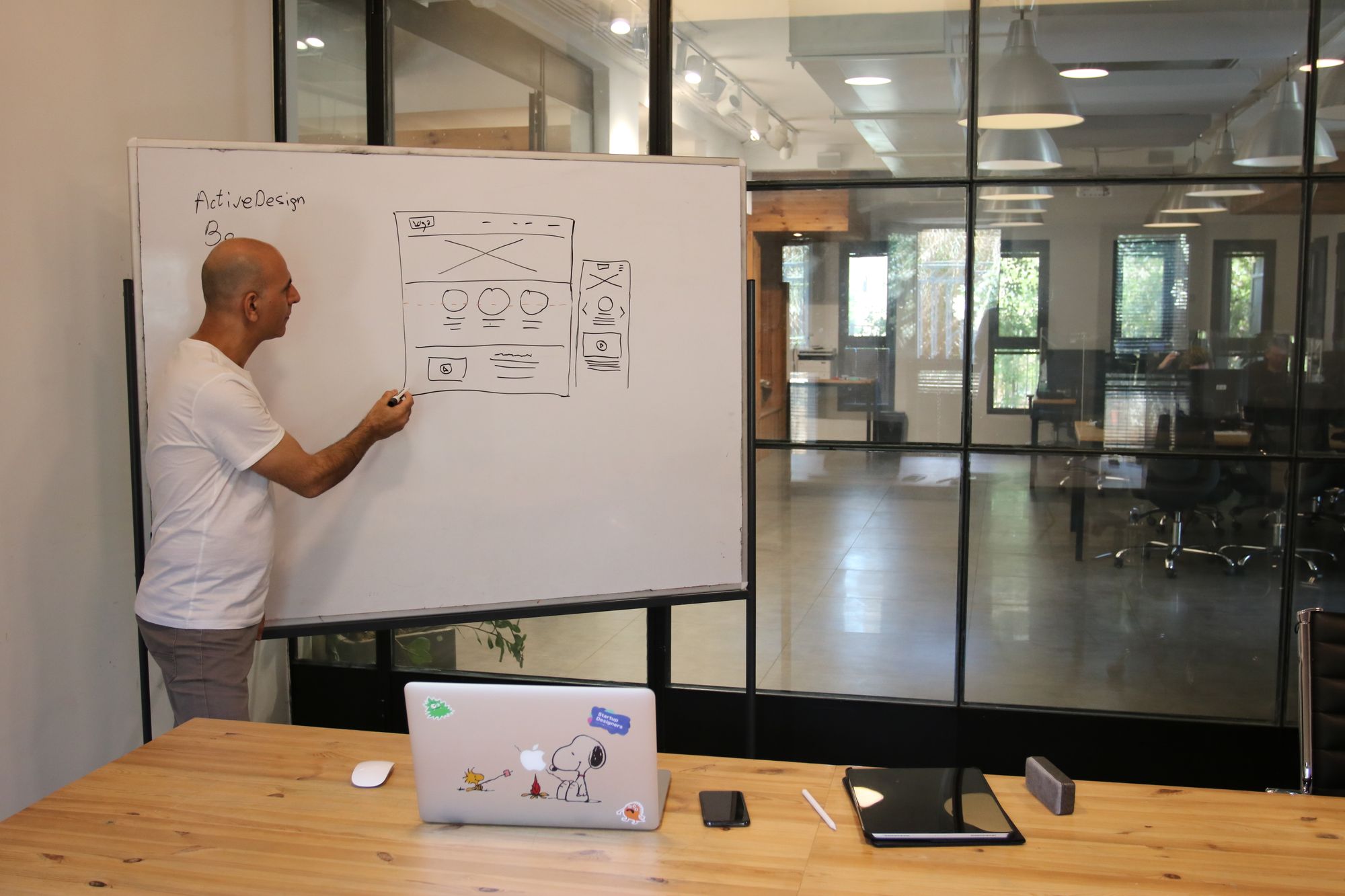 A systems sketch being drawn on a whiteboard beside a wood table